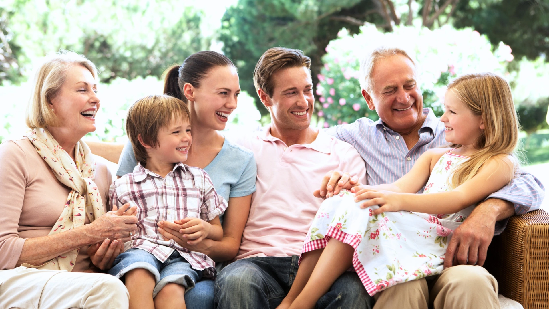 A family with grandparents, parents and children sitting and smiling on a couch outside together discussing the family trust tax change.